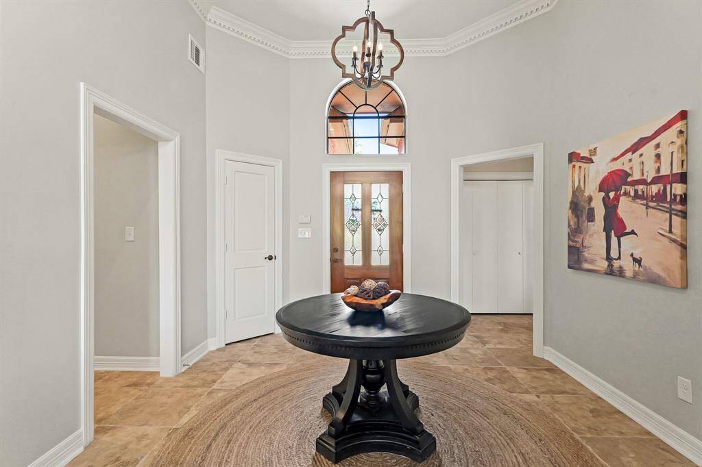 The Foyer is light and bright thanks to the sky-high ceilings and neutral color palette. The space boasts intricate crown molding, cased openings, and durable ceramic tile flooring. The opening to the left leads to two Secondary Bedrooms, while the opening to the right leads to the Primary Retreat.