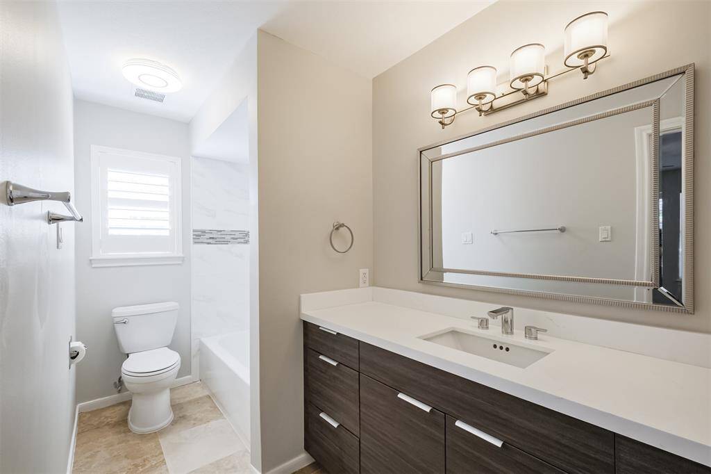 The ensuite bathroom features quartz counters, Kraus sink, energy efficient Grohe faucet, modern tiled bathtub and shower surround, Alvic cabinetry and a window with plantation shutters.