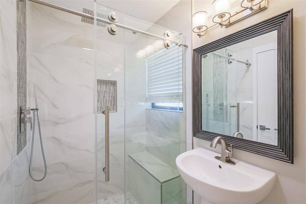 The first floor downstairs full bathroom is ensuite to the flex room allowing lots of options for this space. The stand up shower with bench features a rainfall shower head with handheld sprayer, decorative tile accents and sliding glass door enclosure.