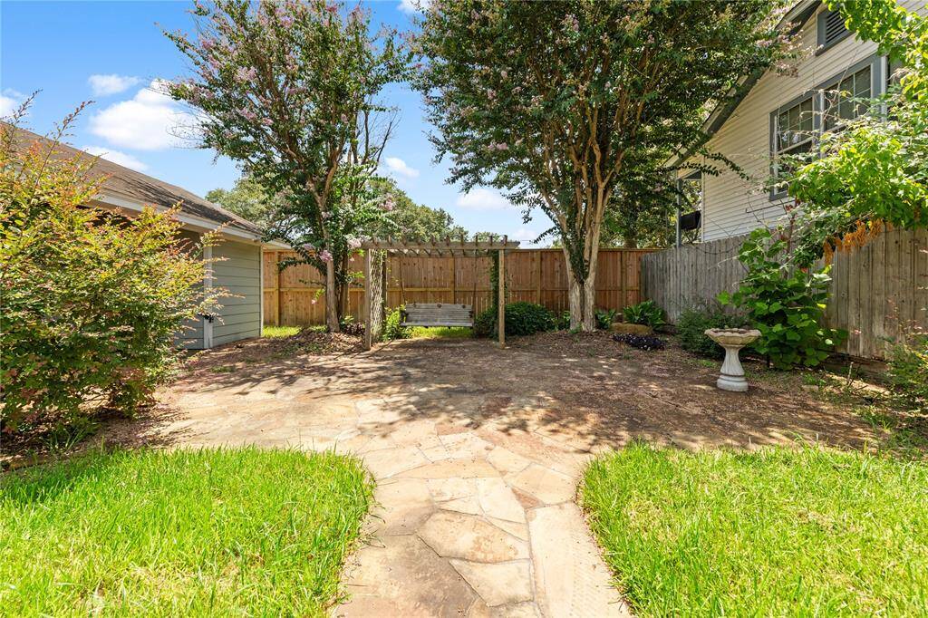 Charming backyard with a stone patio, lush greenery, mature trees, and a wooden fence for privacy. Ideal for relaxation and outdoor gatherings.