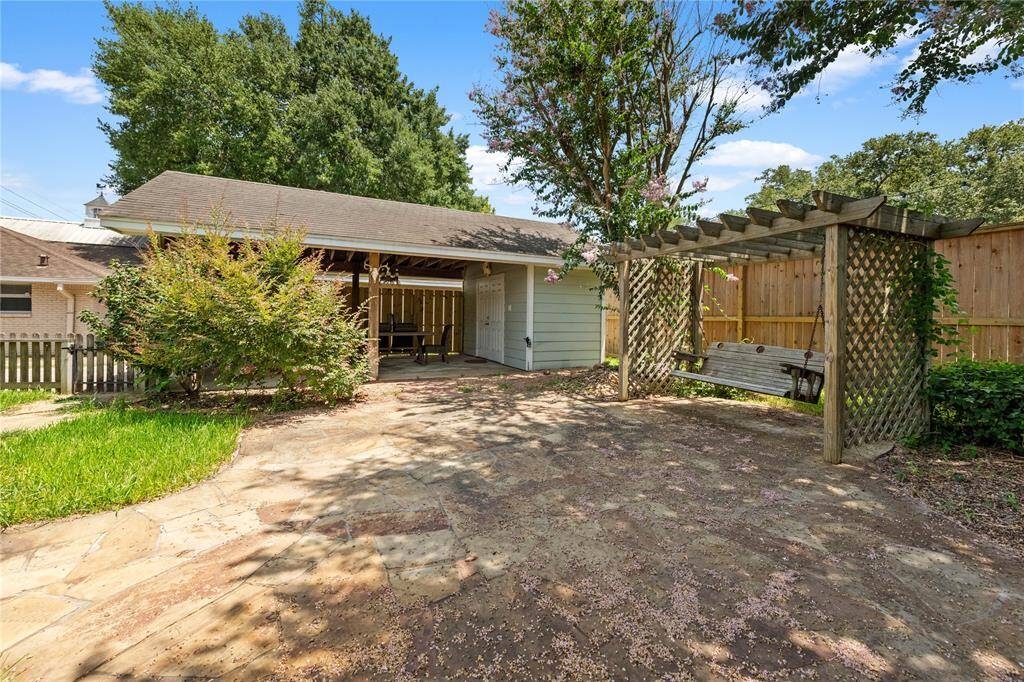 Charming backyard with a covered patio, pergola swing, and paved area surrounded by greenery, perfect for relaxation and entertaining.