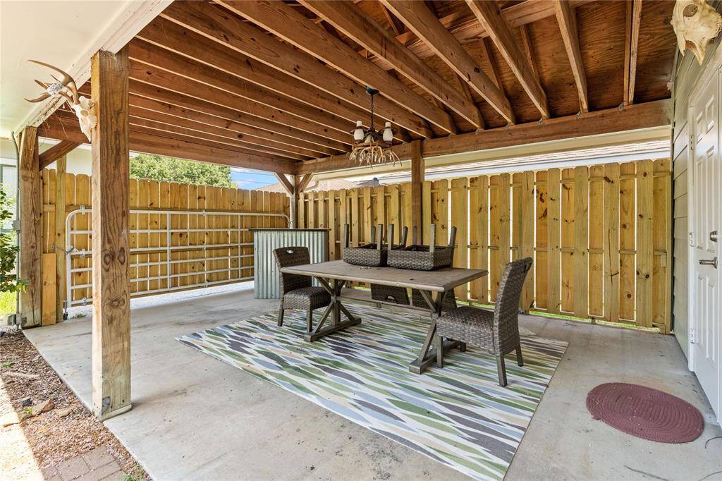 This photo shows a cozy covered outdoor patio with a wooden ceiling and fenced walls, featuring a dining set on a decorative rug, creating an inviting space for outdoor gatherings.