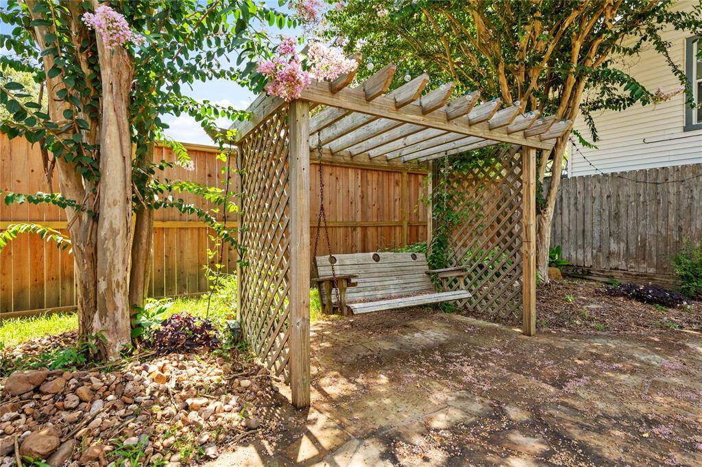 Charming backyard with a wooden pergola and swing, surrounded by a privacy fence and lush greenery, creating a cozy outdoor retreat.