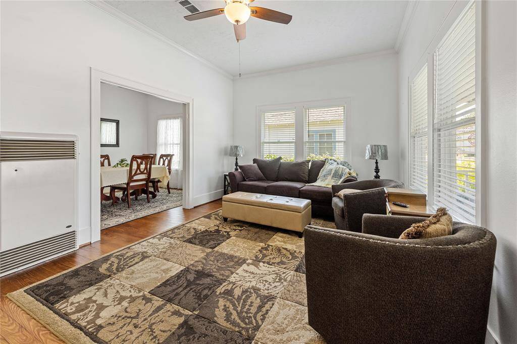This cozy living room features a stylish sectional sofa, large windows for natural light, and a ceiling fan. The open layout leads to a dining area, perfect for entertaining.