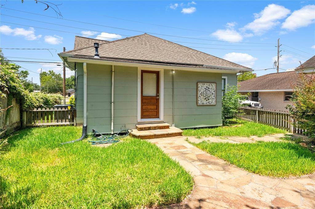 Cozy backyard with a small, charming house featuring a wooden door, surrounded by a well-maintained lawn and a rustic stone pathway, enclosed by a wooden fence for privacy.
