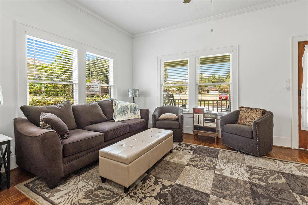 Bright living room with large windows, cozy seating, and a stylish area rug. Features a comfortable sofa, two armchairs, and a cushioned ottoman. Natural light enhances the inviting atmosphere.