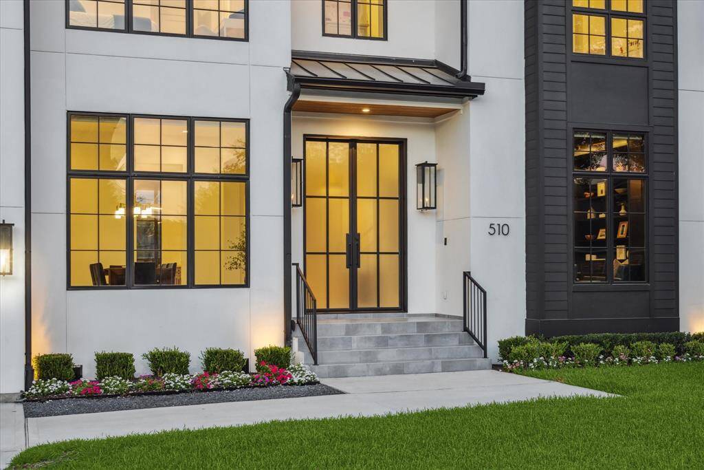 A picture-perfect entrance sets the tone for this custom French Contemporary home, where lush greenery and vibrant flowering beds line the pathway, creating a serene and welcoming approach. The modern glass entry door makes a bold yet graceful statement, inviting you into a space where timeless elegance meets contemporary design.