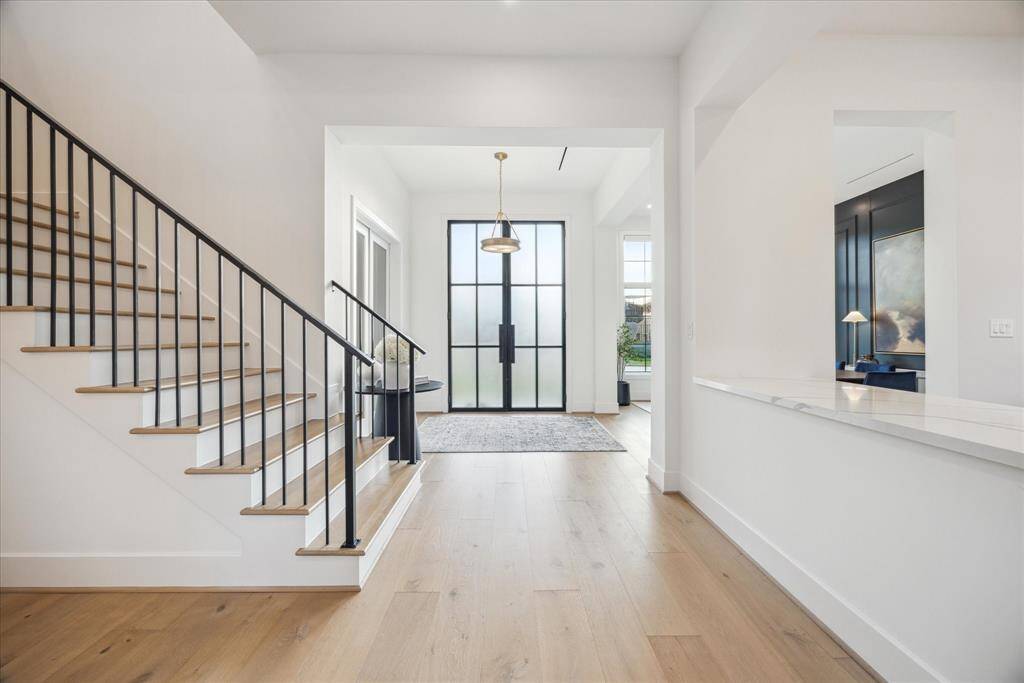 [ENTRANCE] Step inside to a stunning foyer where soaring ceilings, clean architectural lines, and warm wood floors create an immediate sense of refined elegance. Bathed in natural light, the space feels open and airy while maintaining a serene, welcoming ambiance.