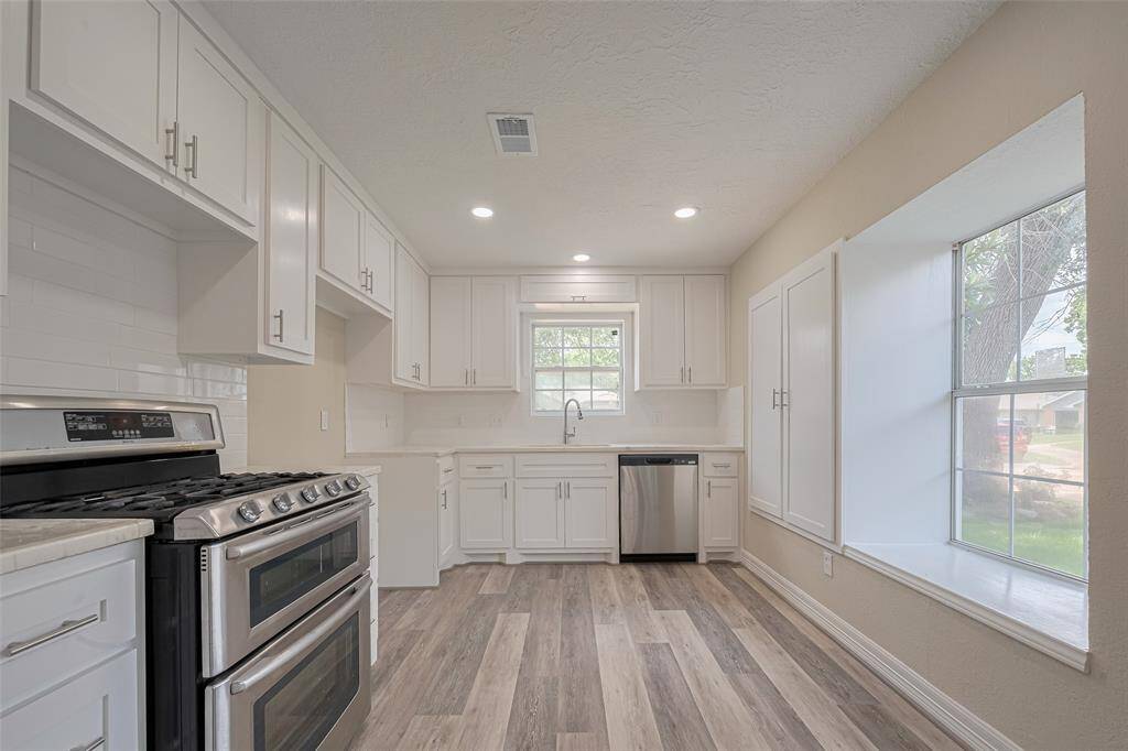 Streamlined and thoughtfully redesigned, the kitchen balances crisp white cabinetry with soft-toned counters and a gently textured backsplash.