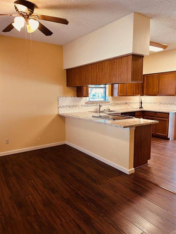 This photo showcases an open kitchen with warm wood cabinetry, granite countertops, and a breakfast bar. The space is complemented by a ceiling fan and dark wood laminate flooring, providing a cozy and functional area for cooking and dining.