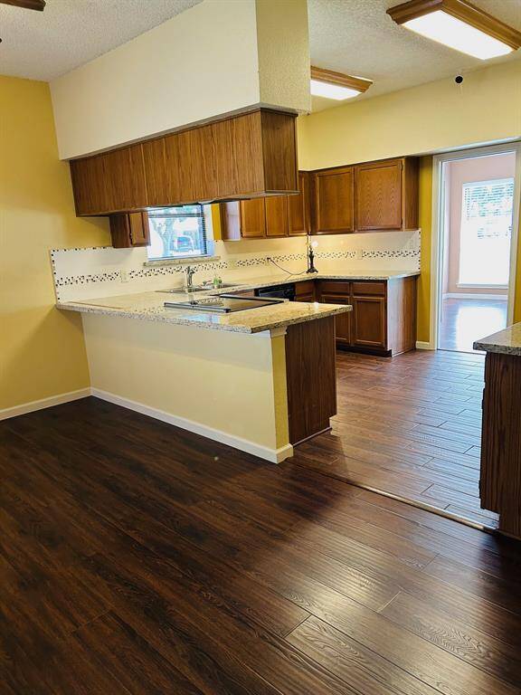 This room features a warm, yellow wall, rich laminate wood flooring, and an open kitchen area with a granite countertop and a small mosaic backsplash. Suitable for a cozy dining space or breakfast nook.