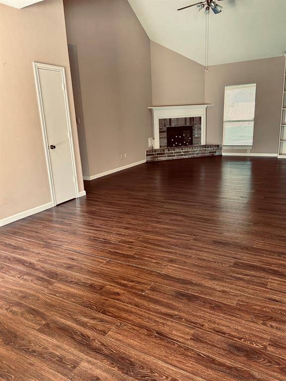 Spacious living room with high ceilings, rich laminate wood flooring, a cozy corner fireplace, and ample natural light from large windows.