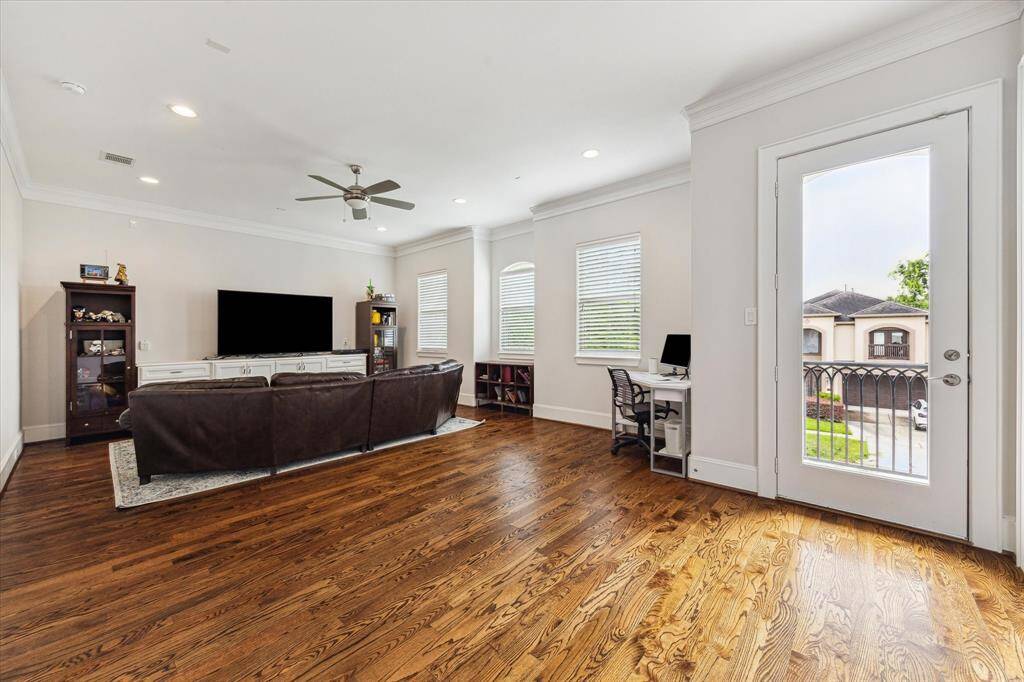 This spacious second floor game room features hardwood floors, recessed lights and built-in bookshelves. Natural light floods in through multiple windows and a glass door leading to a balcony, offering a view of the neighborhood.