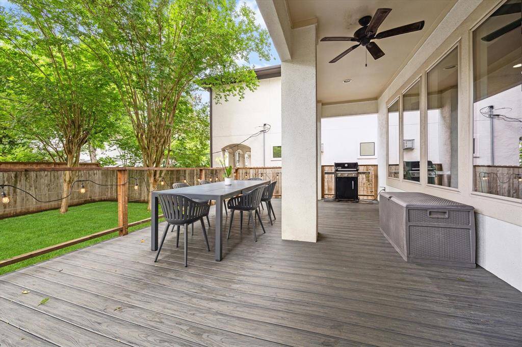 This photo showcases a spacious and inviting covered patio with a ceiling fan, perfect for outdoor dining and entertaining. It features a modern dining set, a grill, and a fenced yard with lush greenery for privacy and relaxation.