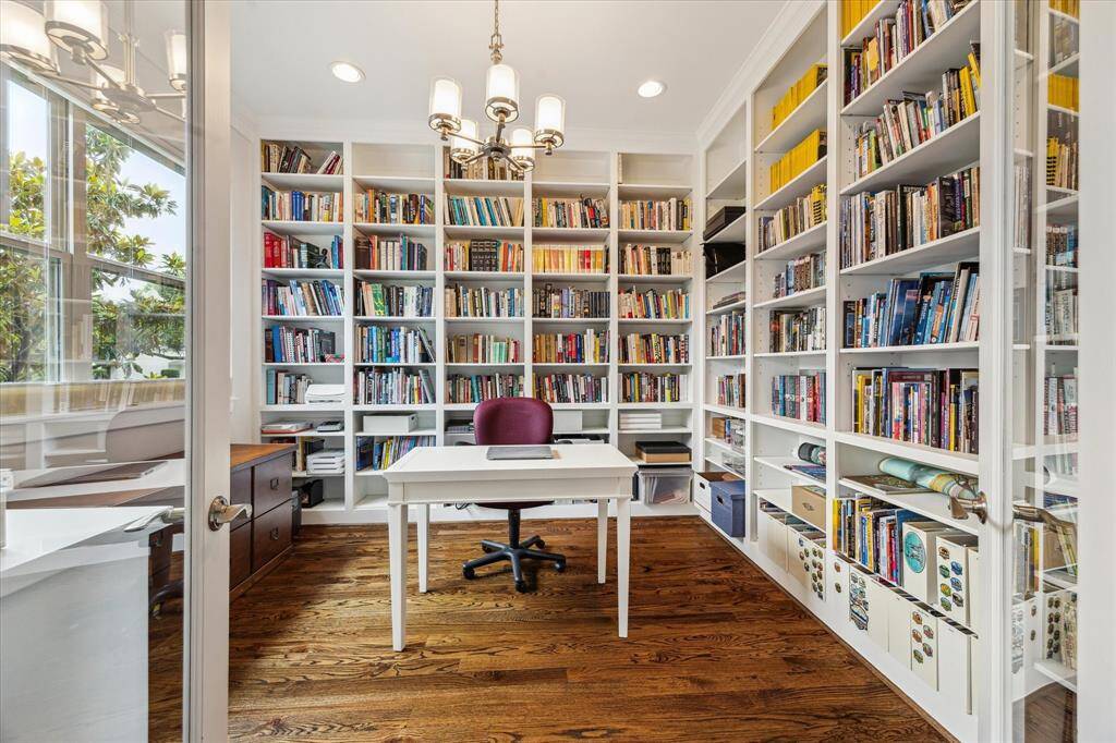 The home office features floor-to-ceiling bookshelves, large windows for natural light and wood flooring, creating a cozy and inviting atmosphere.