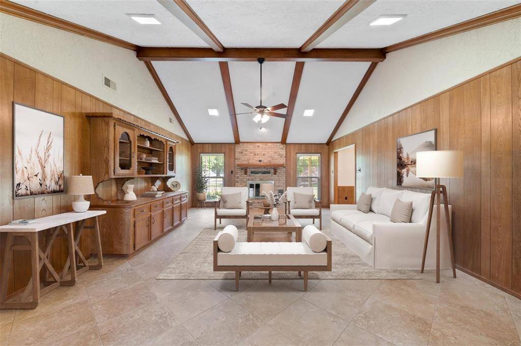 A warm and inviting family room features a classic brick fireplace, custom built-ins, offering both charm and functionality. A rich wood beam spans the vaulted ceiling, adding a rustic touch to this cozy gathering space.