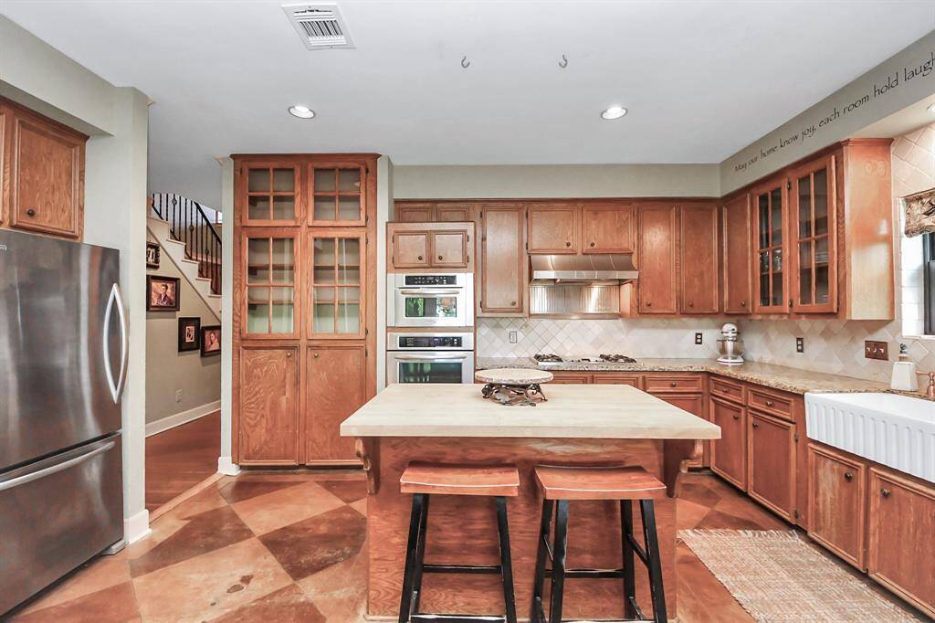This full kitchen view showcases elegant architectural features like glass-door cabinets, a travertine backsplash, and diamond-patterned stained concrete floors with contrasting tones—blending style and functionality.