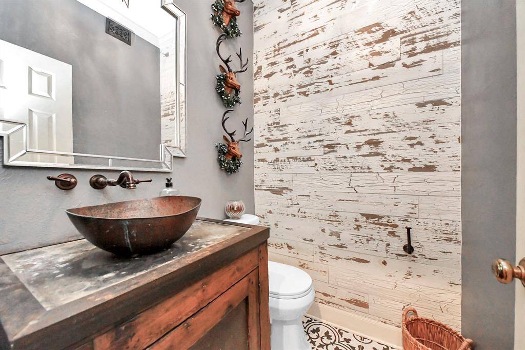 This rustic-modern powder bath showcases a beautifully remodeled design, featuring a copper sink and distressed shiplap wall—blending charm and contemporary style.