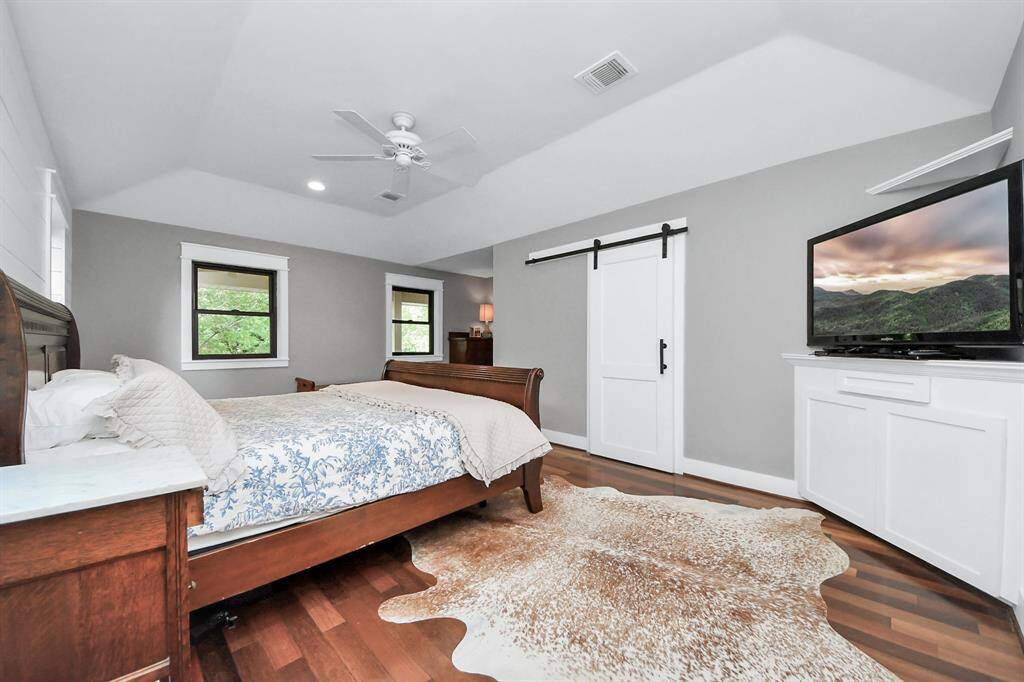 This view of the primary suite highlights a rustic barn door leading to an immense walk-in closet. Angled ceilings add architectural interest and enhance the already generous sense of space.