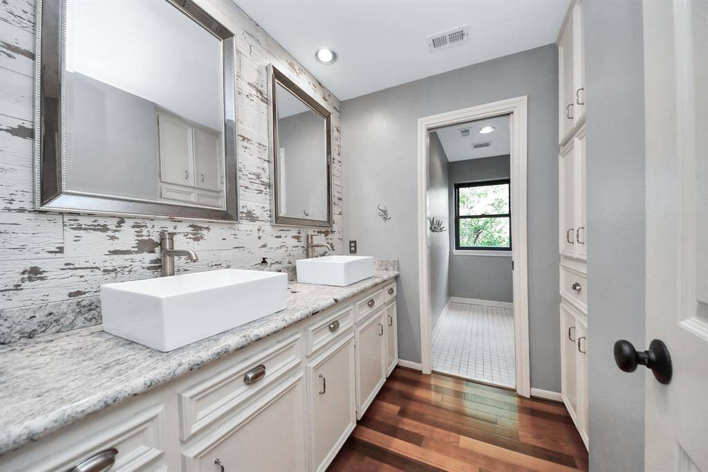 This gorgeous modern secondary bath features square porcelain above-counter sinks, sleek gray quartz counters, and distressed shiplap wall. Silver-framed mirrors add a touch of elegance, while a private area houses the tub/shower combo and commode.