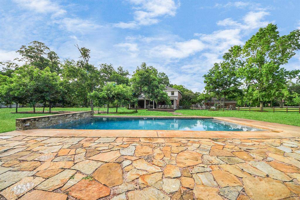 Flagstone decking surrounds the pool, framed by mature trees and an upgraded, fully fenced yard. This view captures the peaceful beauty of the backyard, looking back toward the home’s inviting rear elevation.