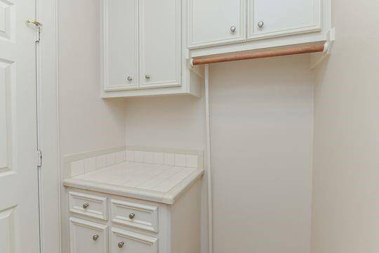 The 2nd floor laundry room features an abundance of cabinets & a folding & hanging space.