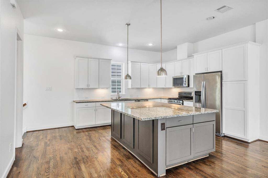 On Second floor,  kitchen features a spacious design with a large island, granite countertops, and modern stainless steel appliances. It has ample white cabinetry and pendant lighting, complemented by warm hardwood floors.