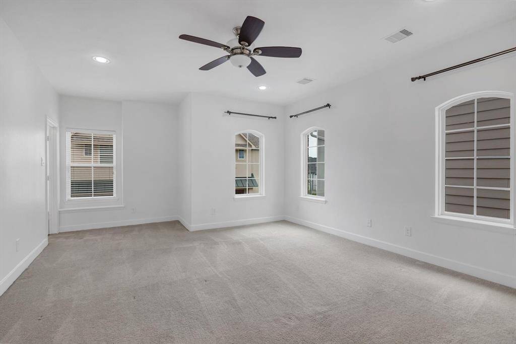 Third floor, spacious primary bedroom with neutral walls, large windows offering natural light and a ceiling fan for comfort.