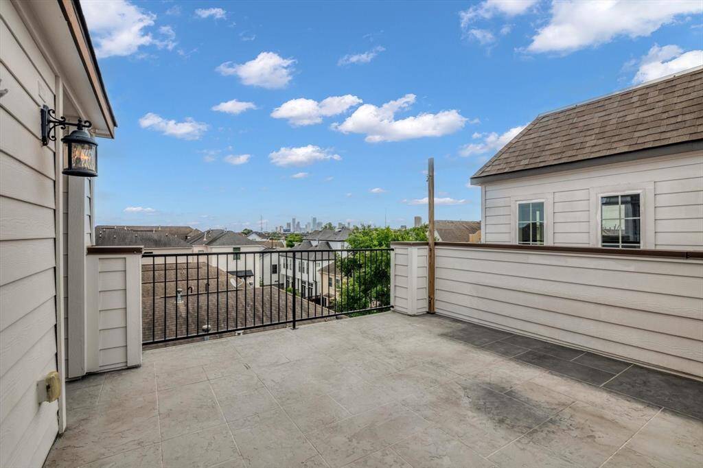 Spacious rooftop terrace with a tiled floor and metal railing, offering a scenic view of the neighborhood and Houston city.