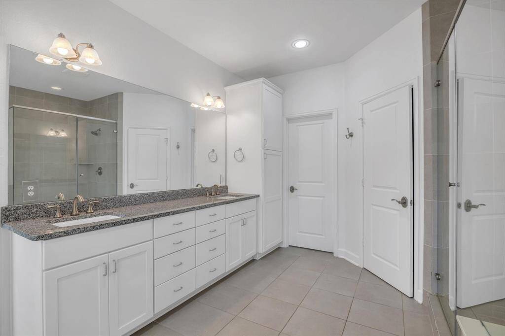 En-suite primary bathroom features a spacious design with dual sinks, a large granite countertop, a large mirror, ample cabinet storage.
