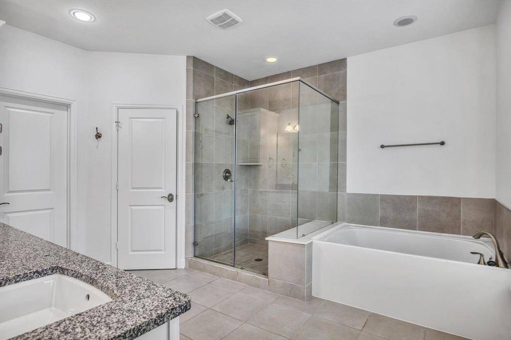 En-suite primary bathroom features a modern design with a spacious glass-enclosed shower, a separate bathtub. The neutral tile and lighting create a bright and inviting space.