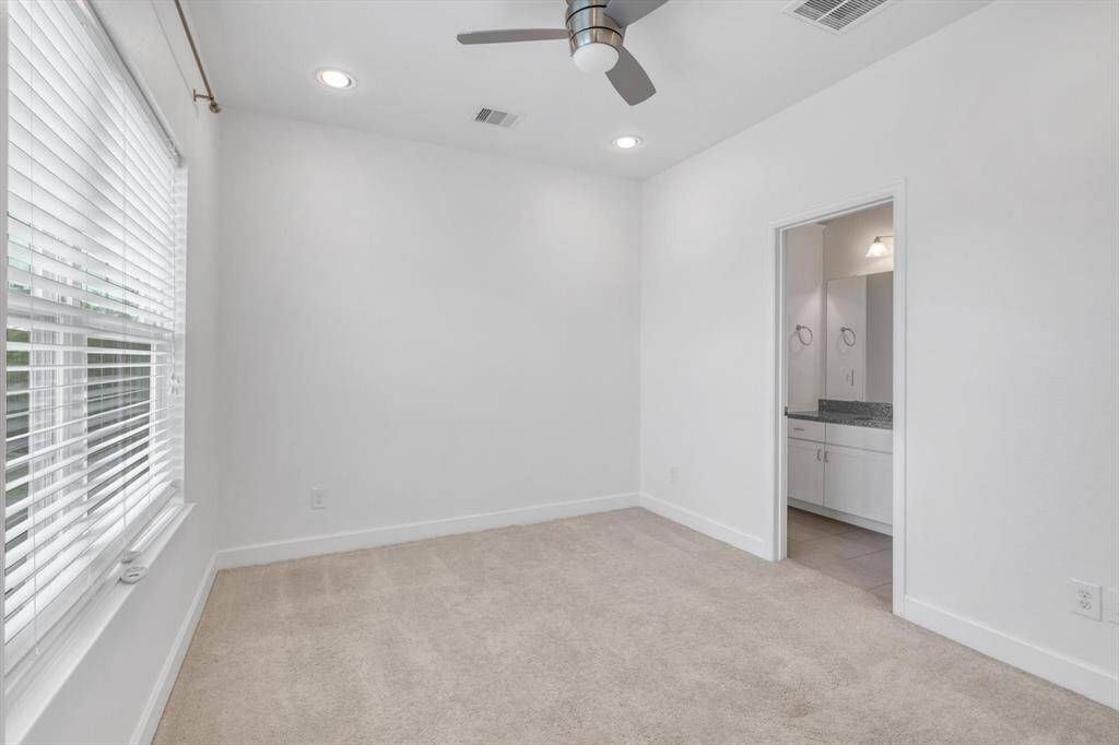 Third floor spacious bedroom with features soft carpet flooring, a ceiling fan, and ample natural light from large windows. It leads into an en-suite bathroom with a modern vanity.