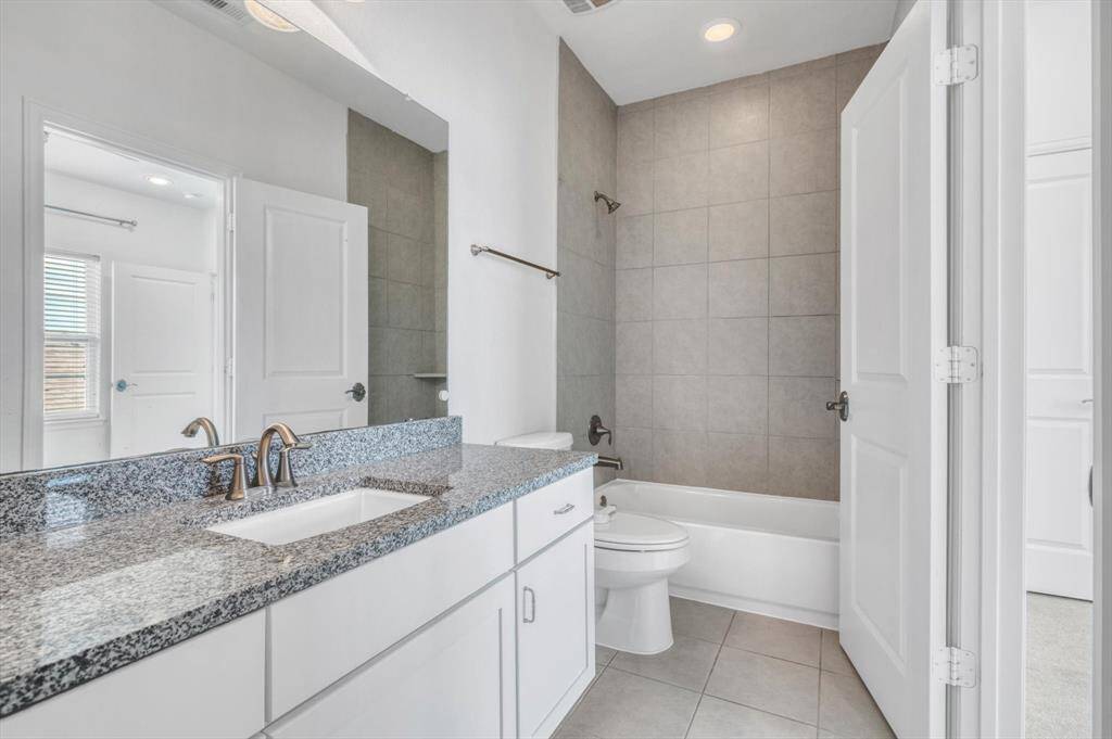 En-suite bathroom features a sleek granite countertop with dual sinks, modern fixtures, and a tiled shower-tub combo. The space is bright and clean, with neutral tones and ample storage.