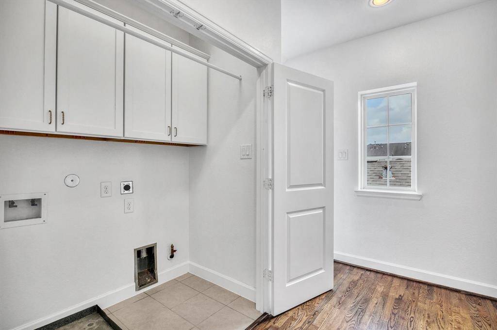 Third Floor, Functional laundry room with white cabinetry, tile flooring in the washing area, and hardwood floors extending into the adjacent space. A window provides natural light, and there are multiple outlets and connections for laundry appliances.