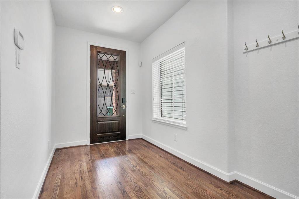 Bright entryway with a stylish wooden door, hardwood floors, and a window with blinds. The space includes wall hooks for convenience.