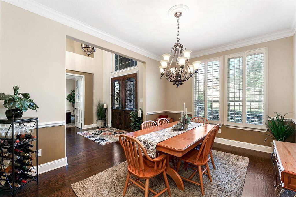Formal dining room with an elegant light fixture, chair rail, crown molding, wood floors, and plantation shutters on the front of the home.