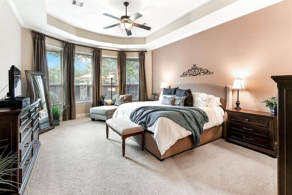 Retreat to a spacious primary bedroom adorned with elegant tray ceilings, bay windows with custom window coverings that flood the room with natural light and a view of the backyard.