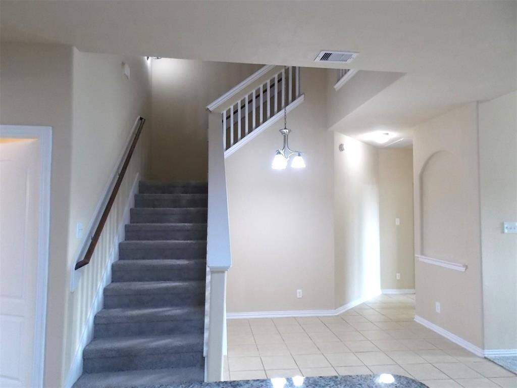 Spacious living room with high ceilings and abundant natural light from multiple windows. Features include a ceiling fan, neutral carpet, and a partial view of a granite countertop.