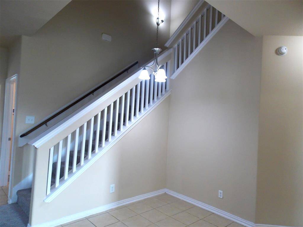 This photo showcases a spacious open-plan living area with carpeted flooring, leading to a modern kitchen featuring granite countertops, white cabinetry, and stainless steel appliances. The space is brightened by large windows and has a tiled entryway, providing a welcoming atmosphere.