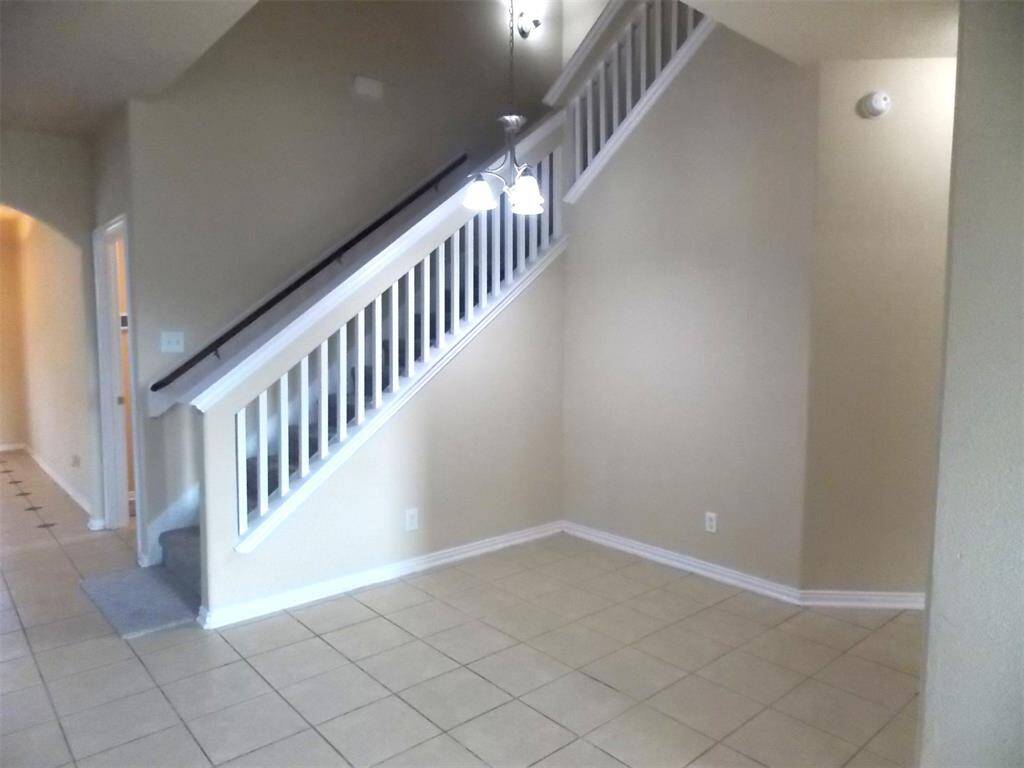 This spacious living area features high ceilings, an open balcony, and a ceiling fan. The kitchen is equipped with modern appliances, granite countertops, and a breakfast bar. There's a mix of carpet and tile flooring, and a staircase leads to the upper level. Natural light enters through large windows, adding to the bright and airy feel.