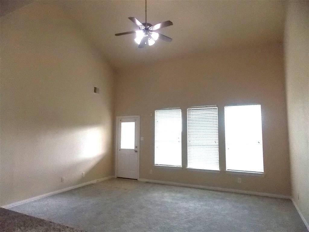 This photo shows a spacious, open-concept kitchen and living area viewed from the staircase. The kitchen features granite countertops, a center island, stainless steel appliances, and tile flooring. The adjacent living area is carpeted with large windows, offering plenty of natural light.
