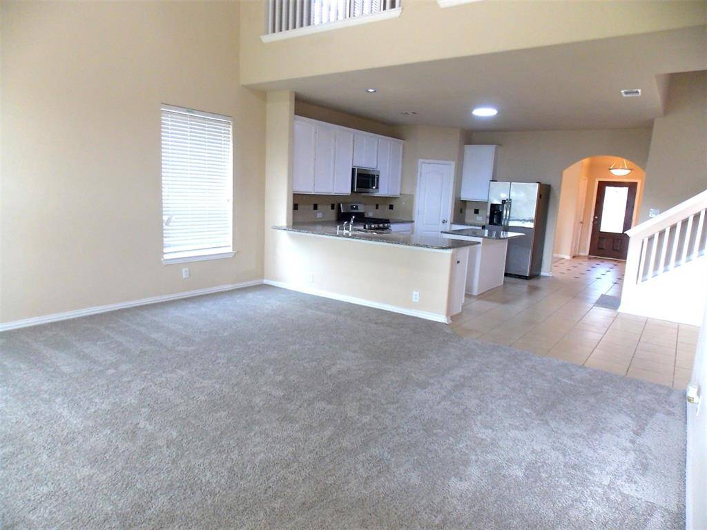 This is a spacious, carpeted room with neutral walls, featuring three large windows with blinds and a ceiling fan with lights, providing ample natural light and ventilation.