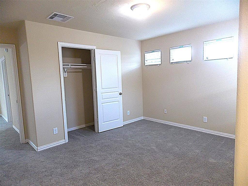 This spacious room features soft carpeting, a ceiling fan with lights, and two windows with blinds, providing ample natural light. The neutral wall color and decorative railing add charm and versatility for various uses.