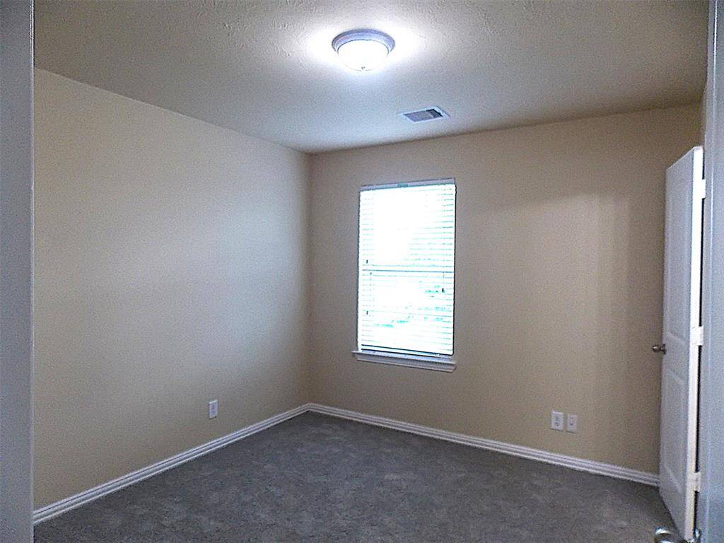 Spacious living room with neutral walls, carpeted flooring, and ample natural light from two windows. Features a ceiling fan and leads to an adjacent room through an open doorway.