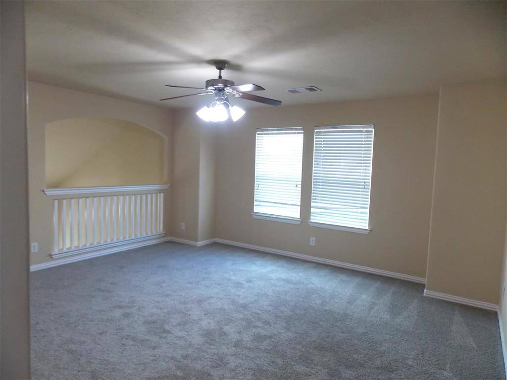 This photo shows a spacious, carpeted room with high ceilings, large windows with blinds, and a ceiling fan with lights. There's a door leading outside, providing natural light and easy access.