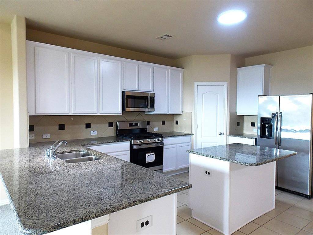 This kitchen features modern stainless steel appliances, including a gas stove and microwave, complemented by granite countertops and ample white cabinetry, offering a clean and functional cooking space.