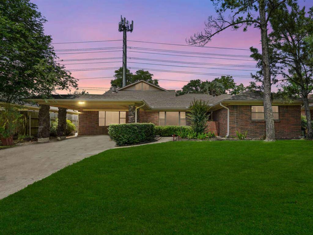 The front elevation features a brick facade, mature landscaping, solid wood front door, and two car carport.