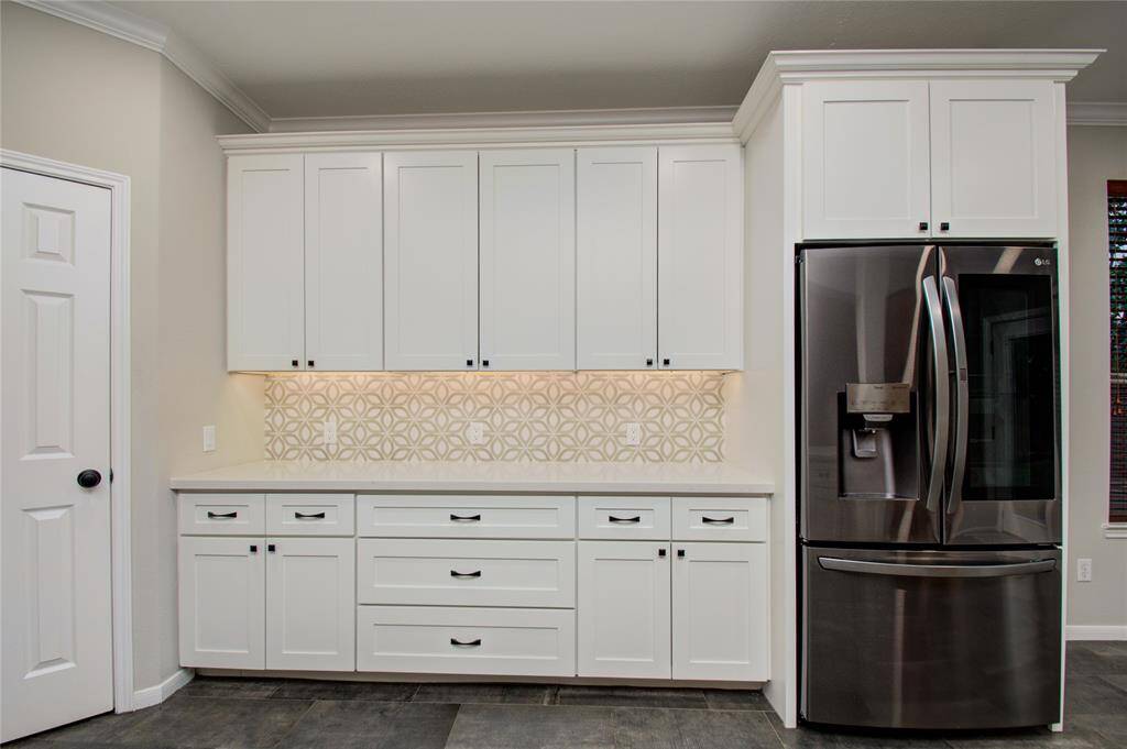 White cabinets, a stylish patterned backsplash, and a stainless steel refrigerator. Ample storage and sleek design create a clean, inviting space.
