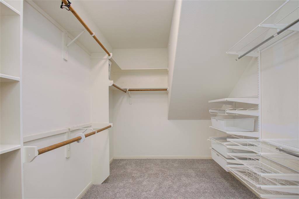 Spacious walk-in closet featuring multiple hanging rods, shelves, and wire basket organizers, ideal for ample storage and organization!
