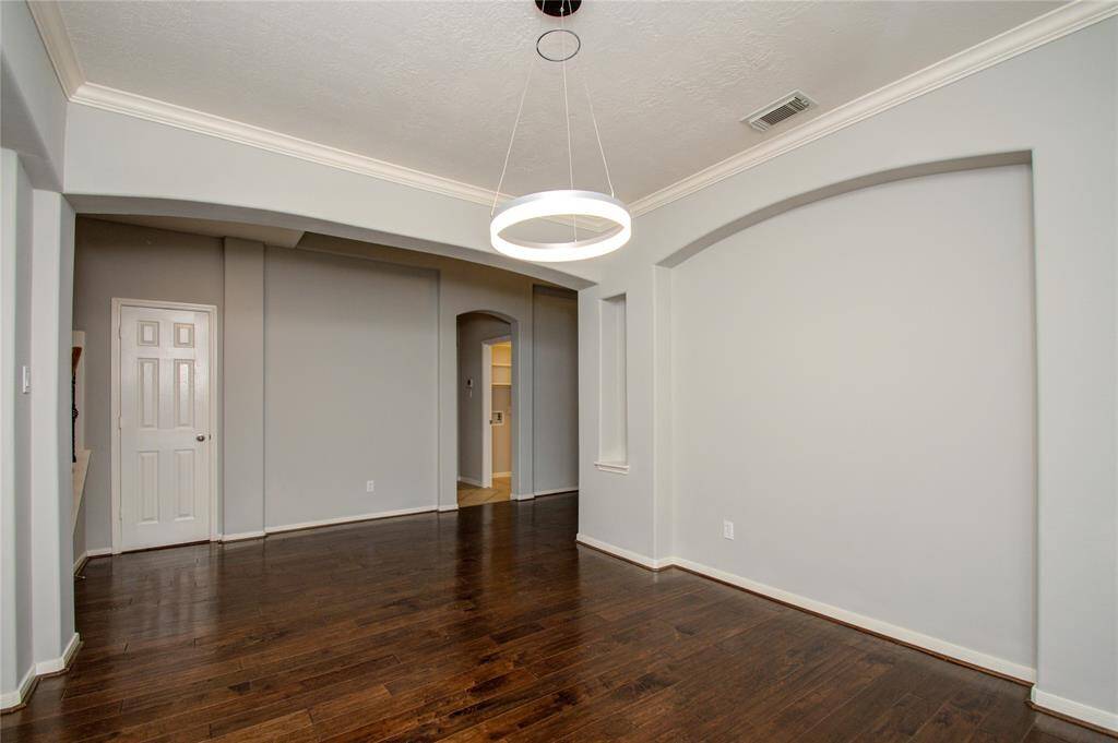 Formal dining room with hardwood floors, light gray walls, and a modern circular light fixture. Arched wall cutouts and crown molding add a refined touch!